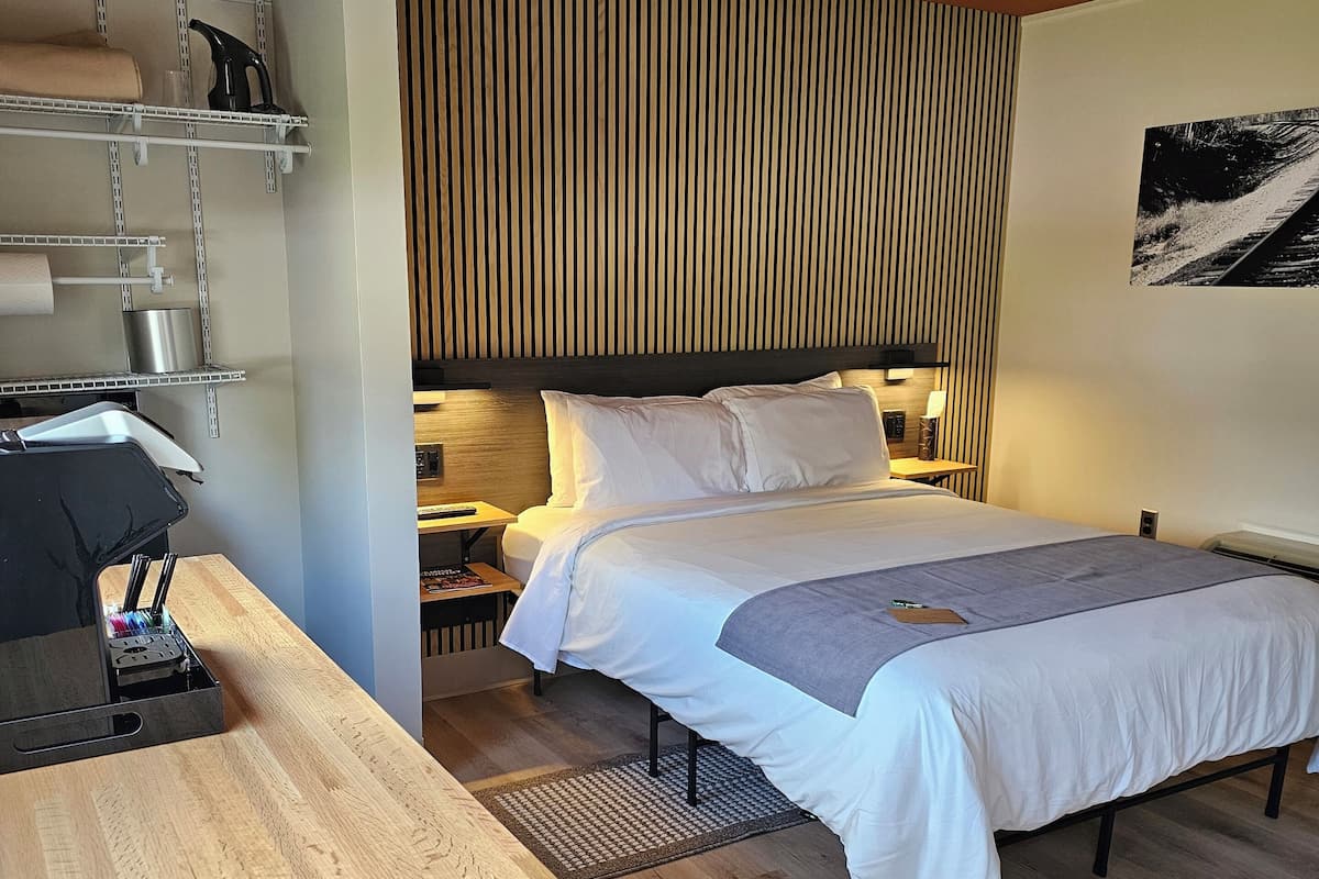 Habitación de hotel con cama, escritorio, estante con artículos de aseo y pared de listones de madera.