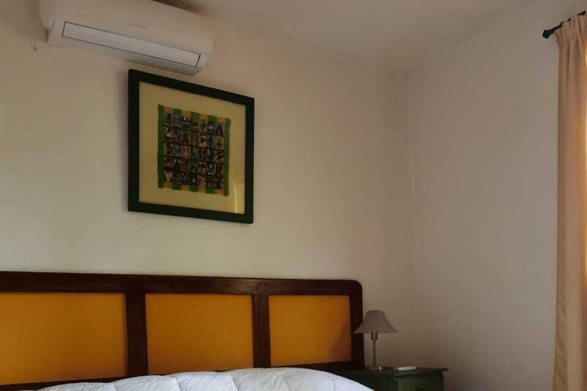 A hotel room with a large bed, a framed picture on the wall, and an air conditioning unit above it.