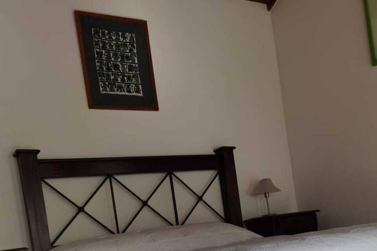 A bedroom with a large bed, a wooden headboard, a nightstand with a lamp, and a framed picture on the wall.