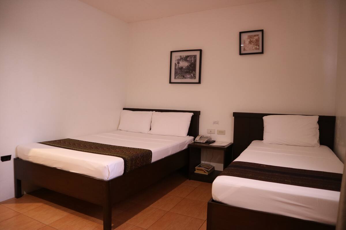 A hotel room with two single beds, a bedside table with a phone and book, and a wall-mounted picture.