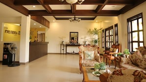 A hotel lobby with a reception desk, floral-patterned sofas, a chandelier, and large windows. - Casa Palmeras Hotel (San Pablo)
