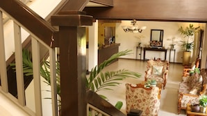 A spacious living area with a high ceiling, a staircase with wooden railings, and a seating area with floral-patterned sofas and a coffee table. - Casa Palmeras Hotel (San Pablo)