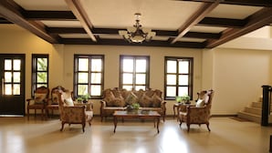 A spacious living room with a large sofa, multiple armchairs, a coffee table, and large windows allowing natural light. - Casa Palmera Tourist Inn (San Pablo)