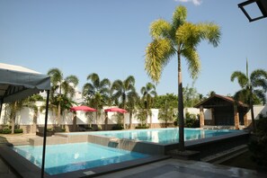 Un espace piscine comprenant plusieurs bassins, des palmiers et des parasols.