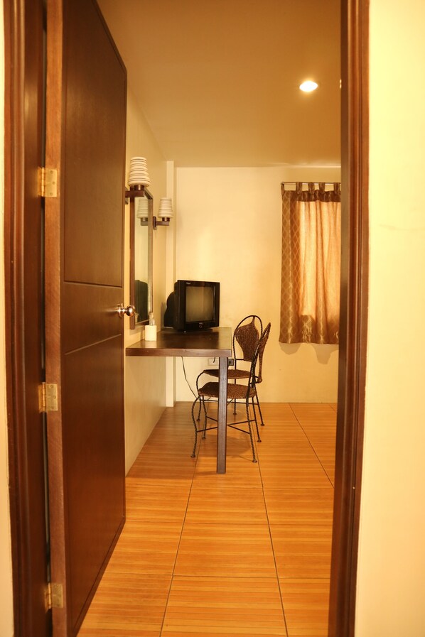 Une pièce avec une porte en bois, une petite table avec une chaise, un téléviseur et un miroir au mur.