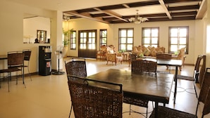 A spacious dining area with a high ceiling, large windows, and wicker furniture. - Casa Palmera Tourist Inn (San Pablo)