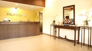 A reception area with a wooden reception desk, a clock, and a mirror above it. There are decorative items on the table and a wall clock. - Casa Palmera Tourist Inn (San Pablo)