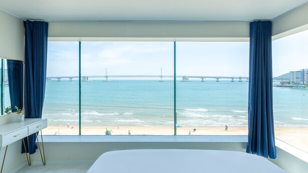 Ein Schlafzimmer mit großem Fenster mit Blick auf einen Strand und eine Brücke.