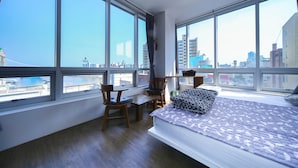 Ein Schlafzimmer mit einem großen Bett, einem Schreibtisch, zwei Stühlen und Blick auf die Stadt durch große Fenster.