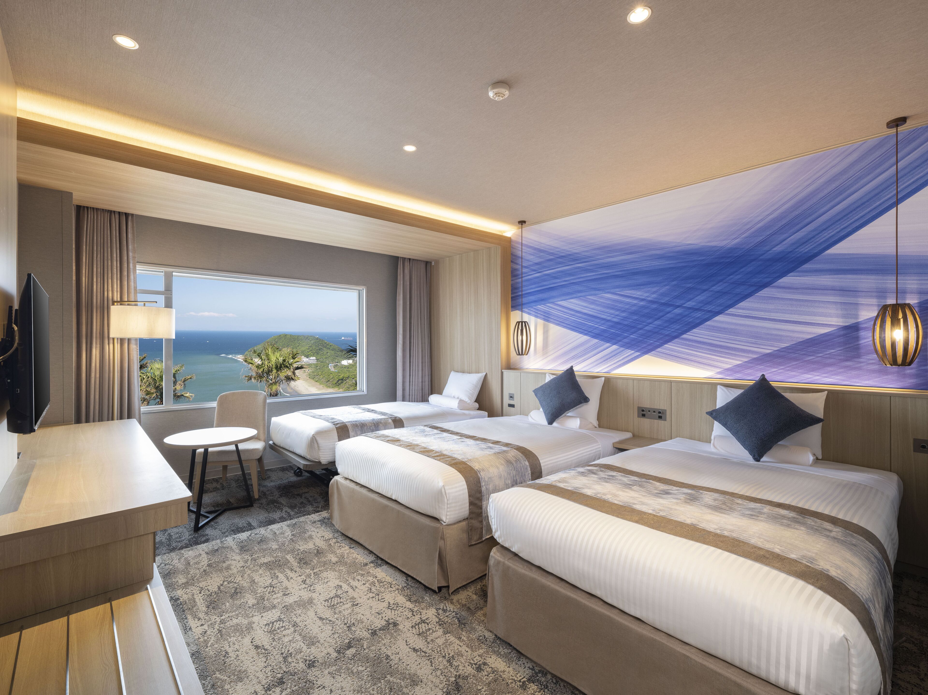 Habitació d'hotel amb dos llits, un escriptori, una cadira i un finestral gran que ofereix vistes a l'oceà.
