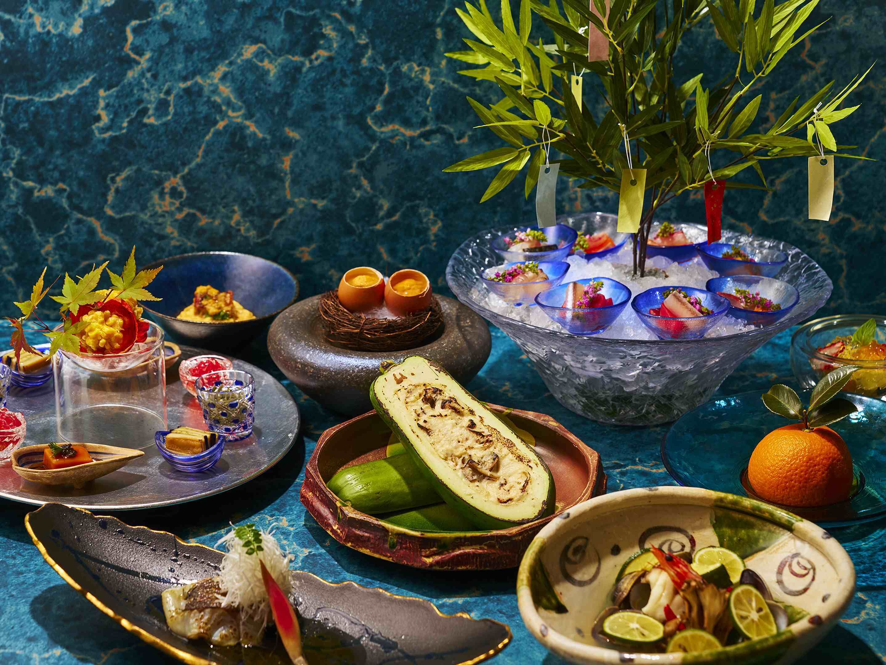 Une variété de plats et de boissons sont proposés, notamment un bol de glace avec des boissons colorées, une assiette avec une demi-portion de fruits coupés et un bol de légumes en tranches.