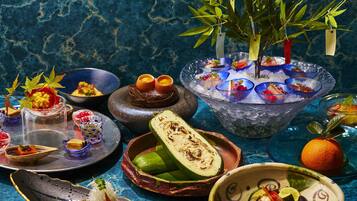A variety of dishes and drinks, including a bowl of ice with colorful drinks, a plate with a half-cut fruit, and a bowl with sliced vegetables.