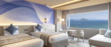 Habitación de hotel con dos camas, zona de estar y un ventanal con vista al mar.