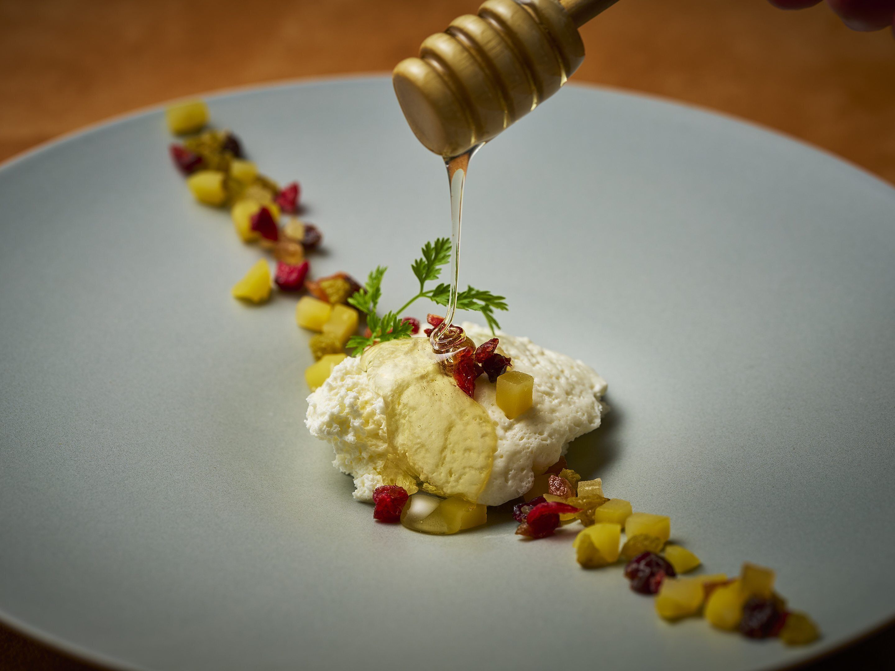 Ein Dessert mit Honig, der auf einen Teller mit Obst und Kräutern geträufelt wird.