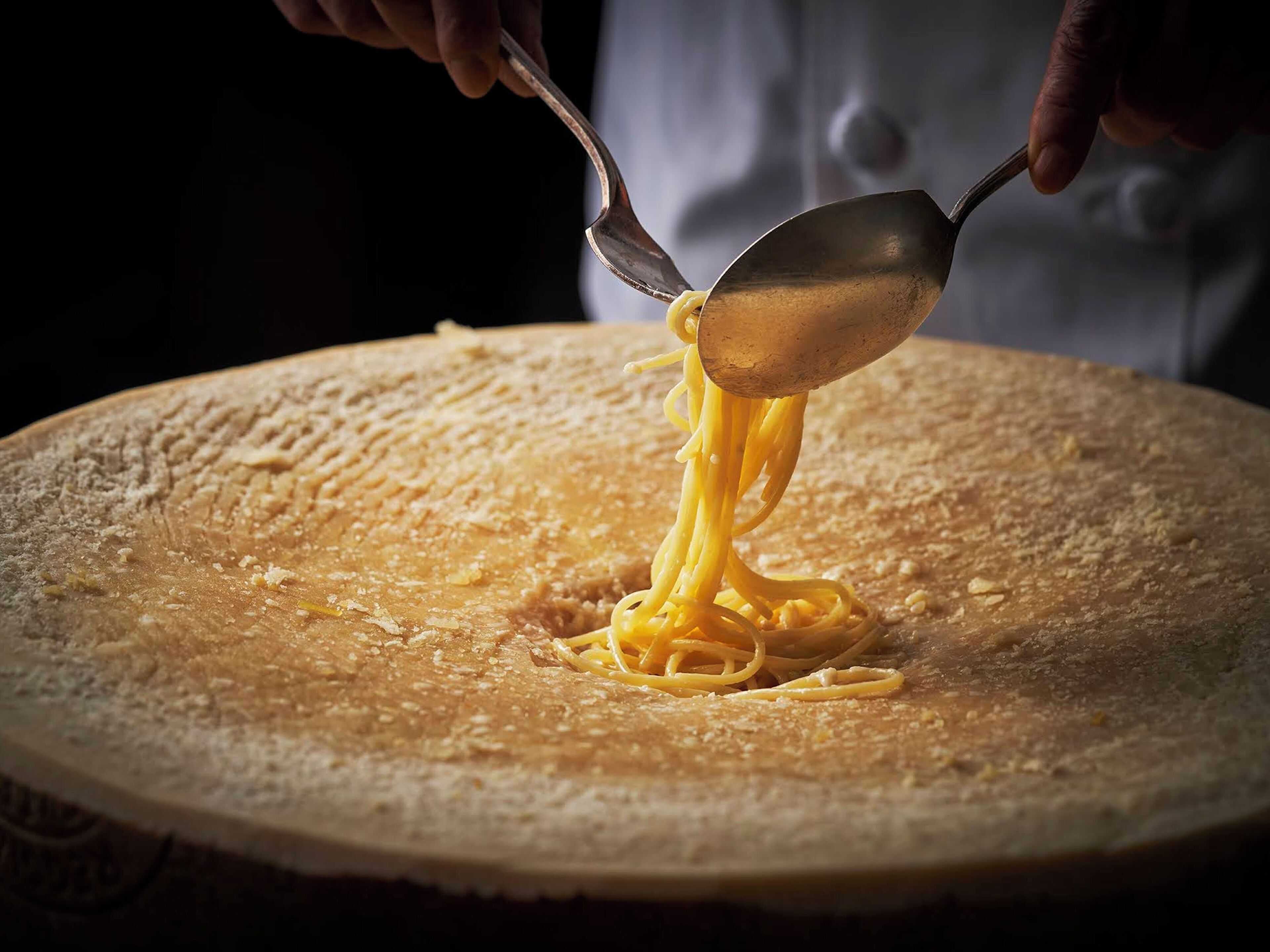 A person using a ladle to serve spaghetti from a large, round, flat surface.