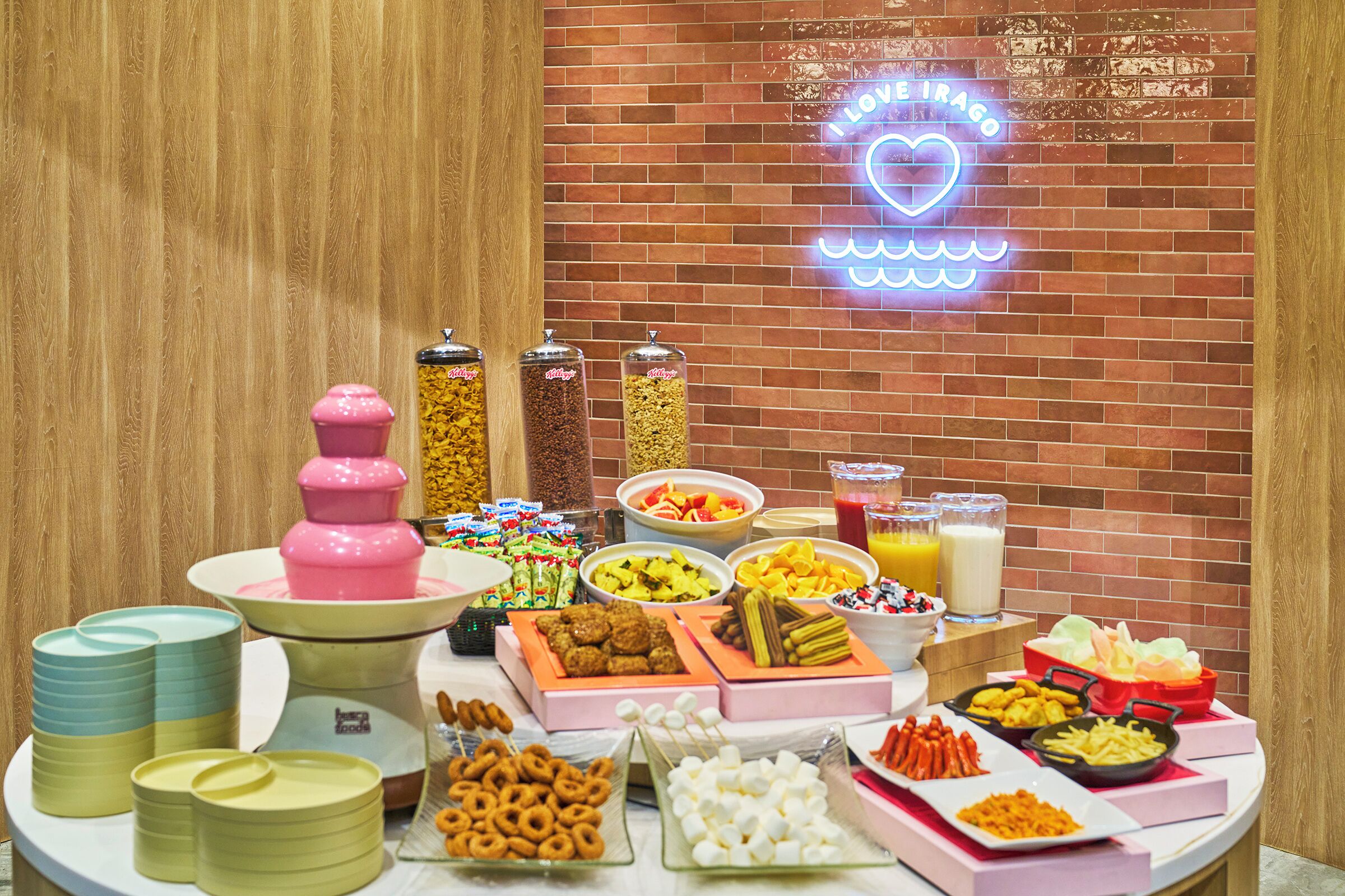 A buffet table with various food items and a neon sign in the background.