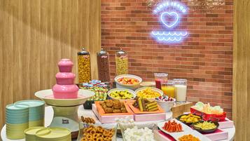 A buffet table with various food items and a neon sign in the background.