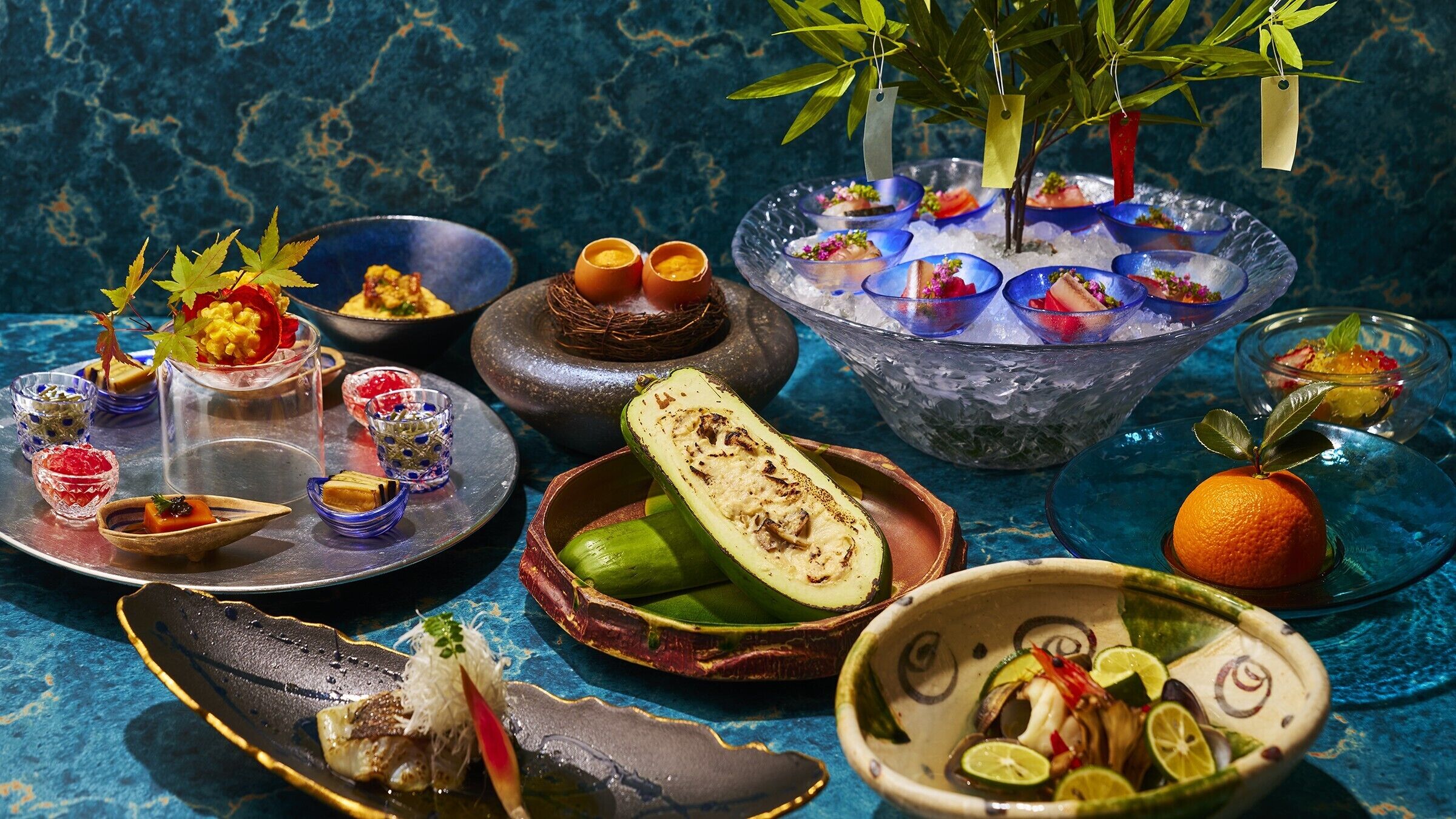 A variety of dishes and a decorative plant on a table with a blue textured background.