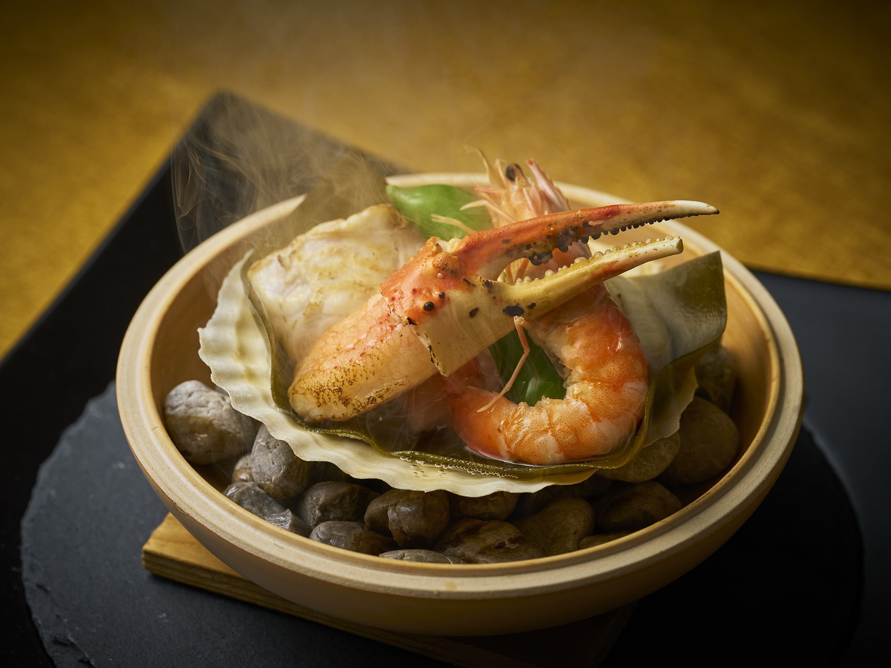 A bowl of seafood with a lobster and shrimp, served on a bed of small round objects.