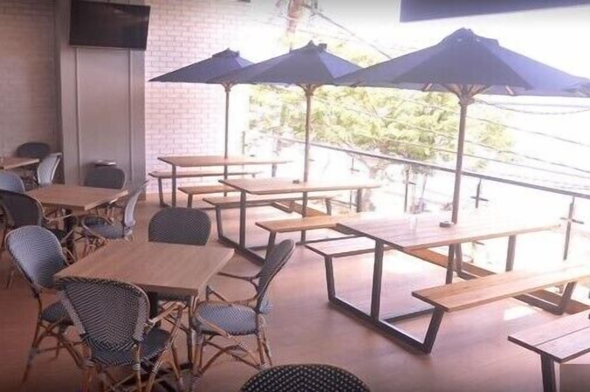 An outdoor cafe with wooden tables and chairs, and blue umbrellas providing shade.