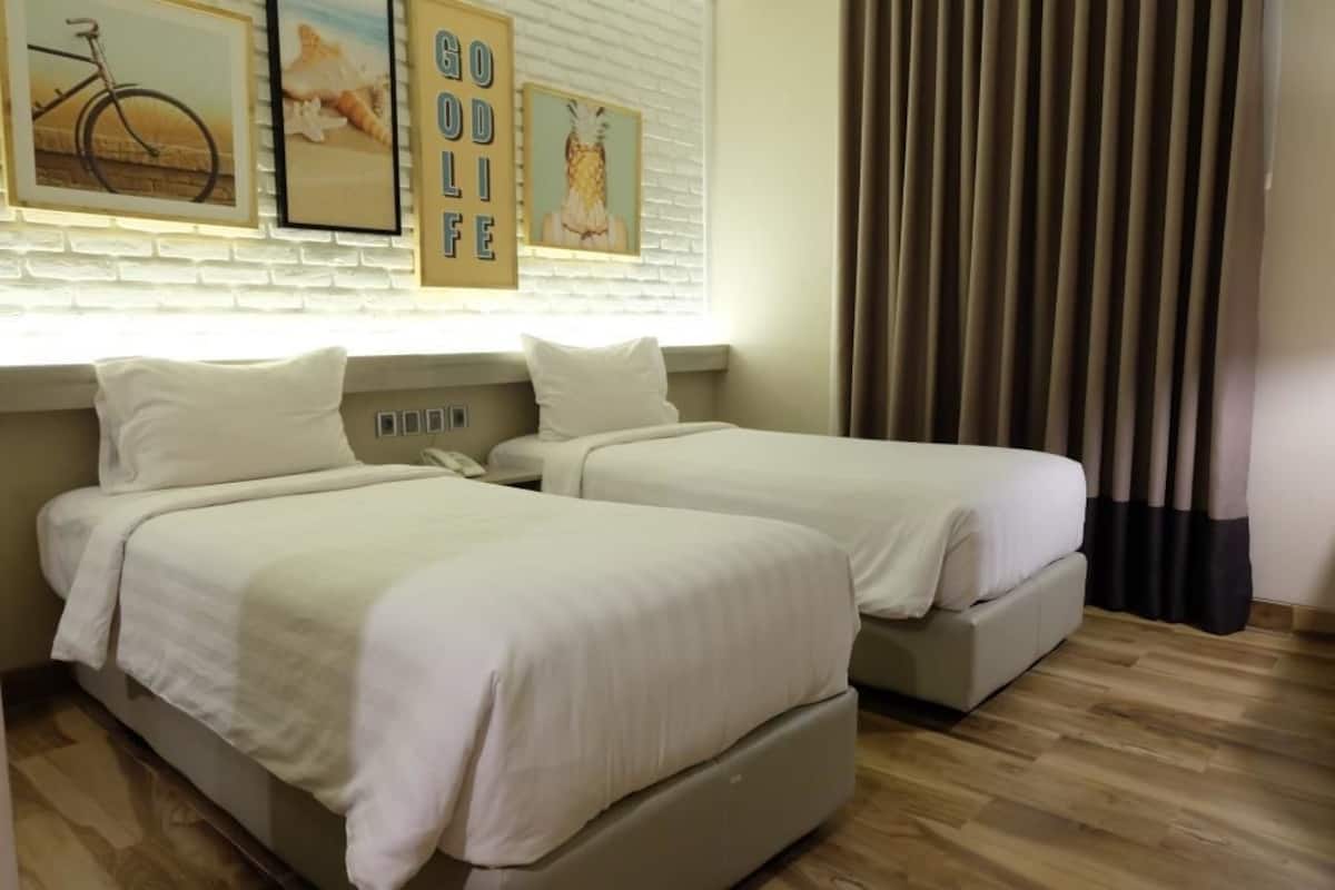 Quarto de hotel com duas camas, parede de tijolos brancos e quadros enquadrados.