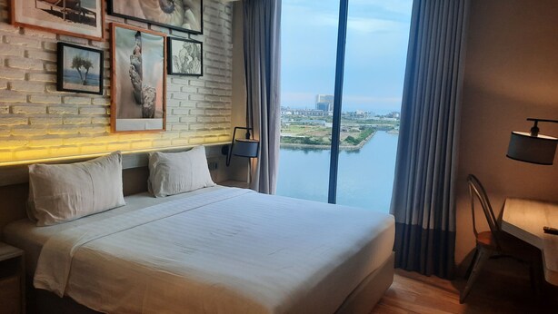 Une chambre d’hôtel avec un grand lit, une vue sur une rivière et sur la ville, et un mur de briques orné de tableaux encadrés.