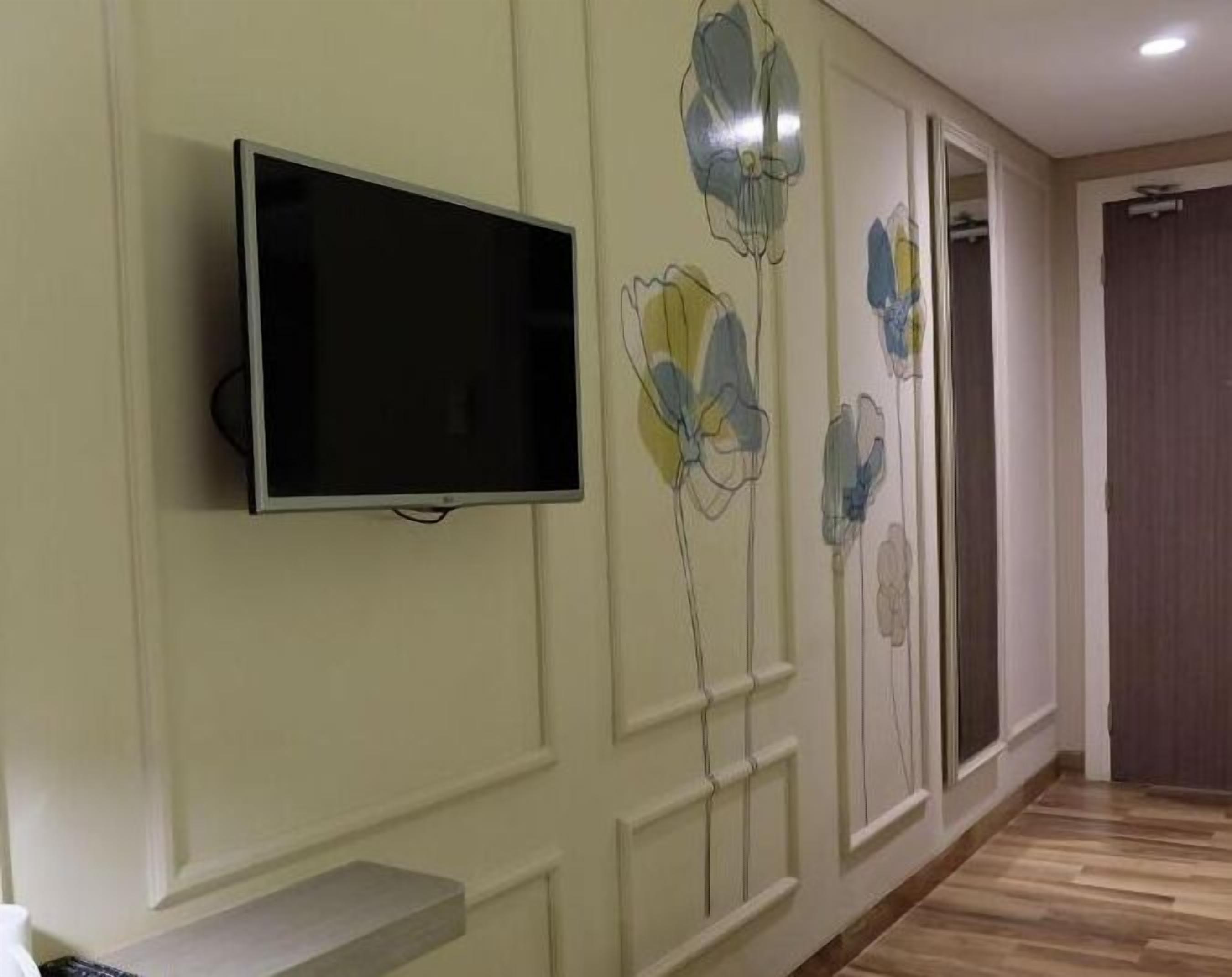 A room with a flat-screen TV mounted on the wall, a wooden floor, and a door on the right.