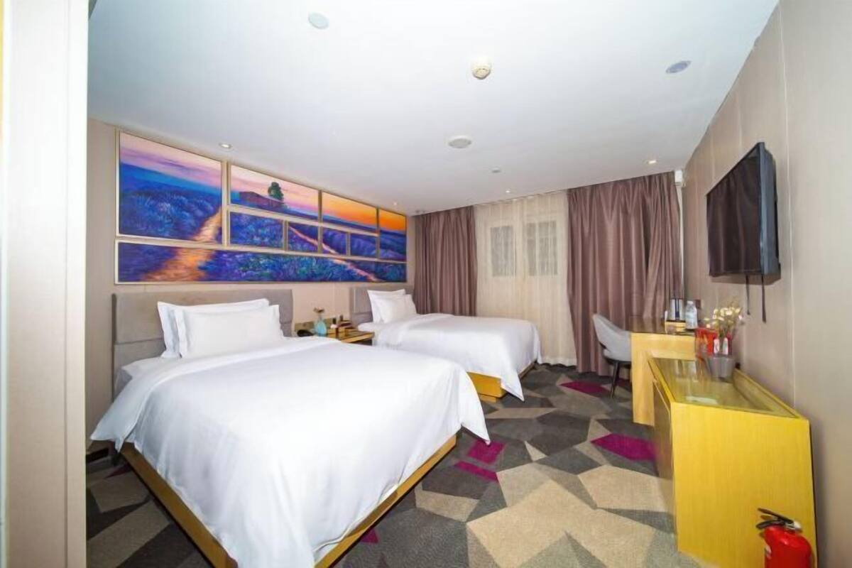 A hotel room with two beds, a desk, a TV, and a painting on the wall.