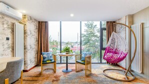 A modern room with a large window, a hanging chair, a round table with chairs, and a sofa. - Ease Cloud Hotel (Beijing)