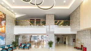 A spacious lobby with a high ceiling, marble flooring, and a modern chandelier. There are seating areas with sofas and tables, and a large potted plant in the center. - Ease Cloud Hotel (Beijing)