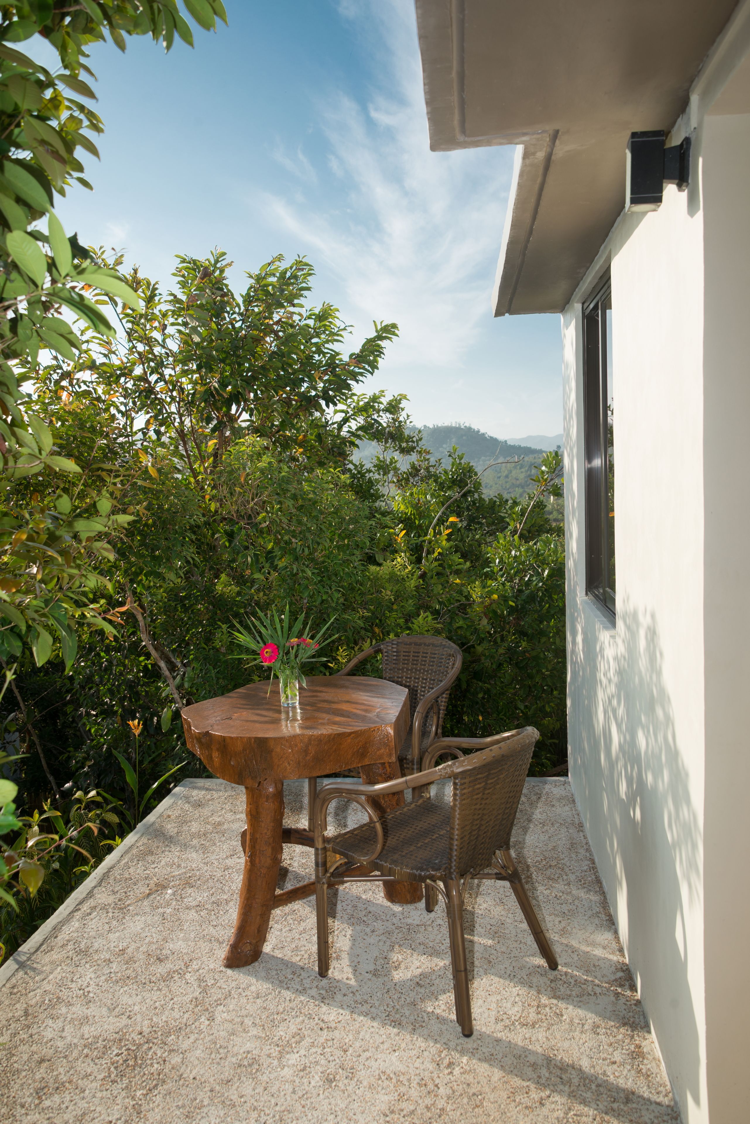 A wooden table and chair set on a balcony with a view of greenery and hills in the background.