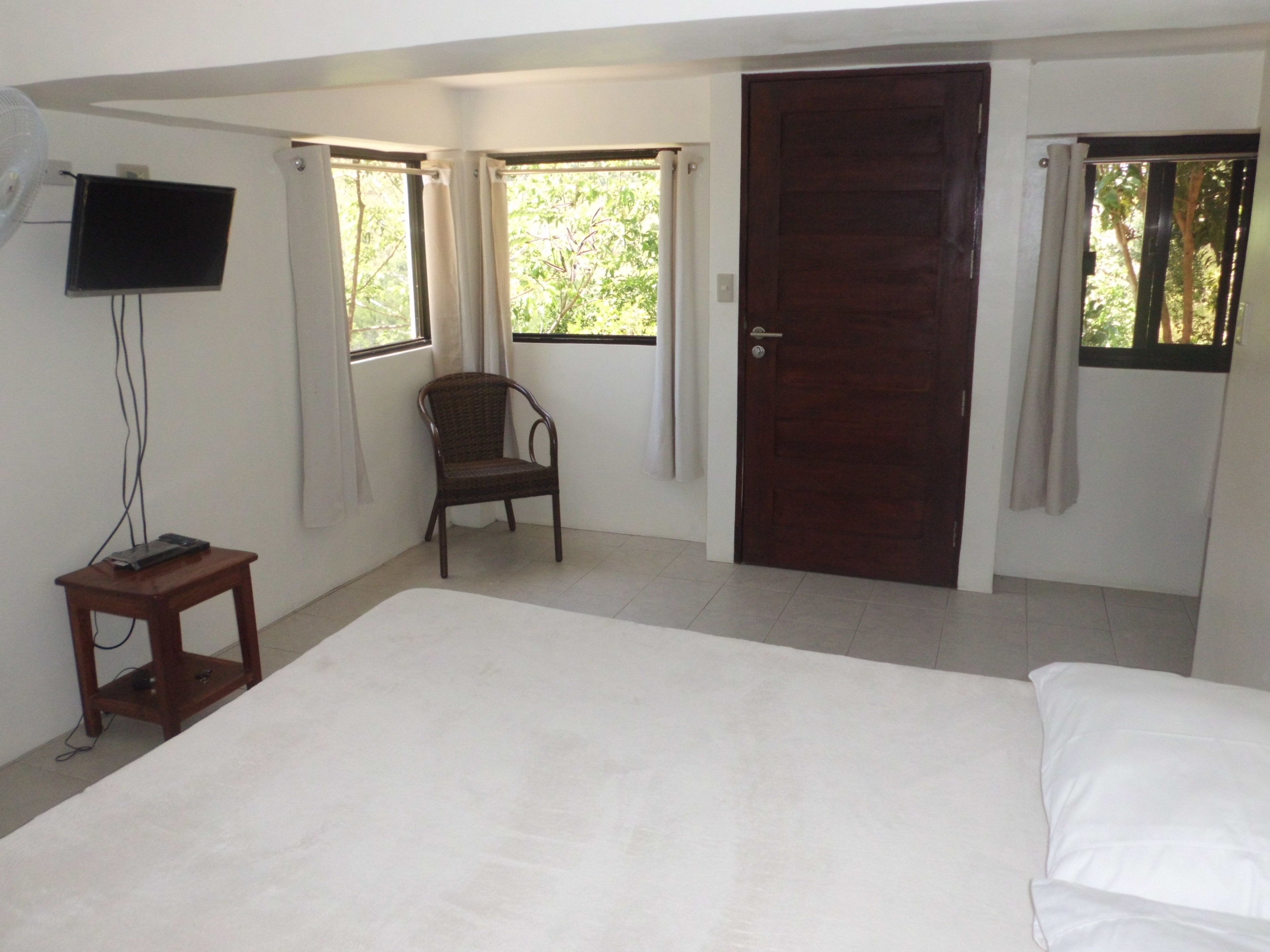 A bedroom with a bed, a chair, a TV mounted on the wall, and a door.