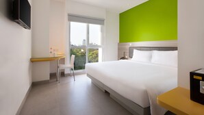 Une chambre d’hôtel moderne équipée d’un lit, d’un bureau, d’une chaise et d’un téléviseur fixé au mur.