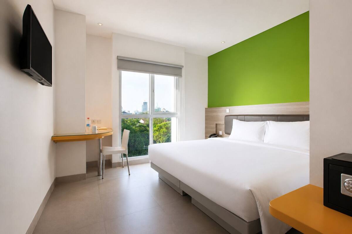 Une chambre d’hôtel équipée d’un lit, d’un bureau, d’une chaise, d’une télévision et d’une fenêtre donnant sur un paysage agréable.