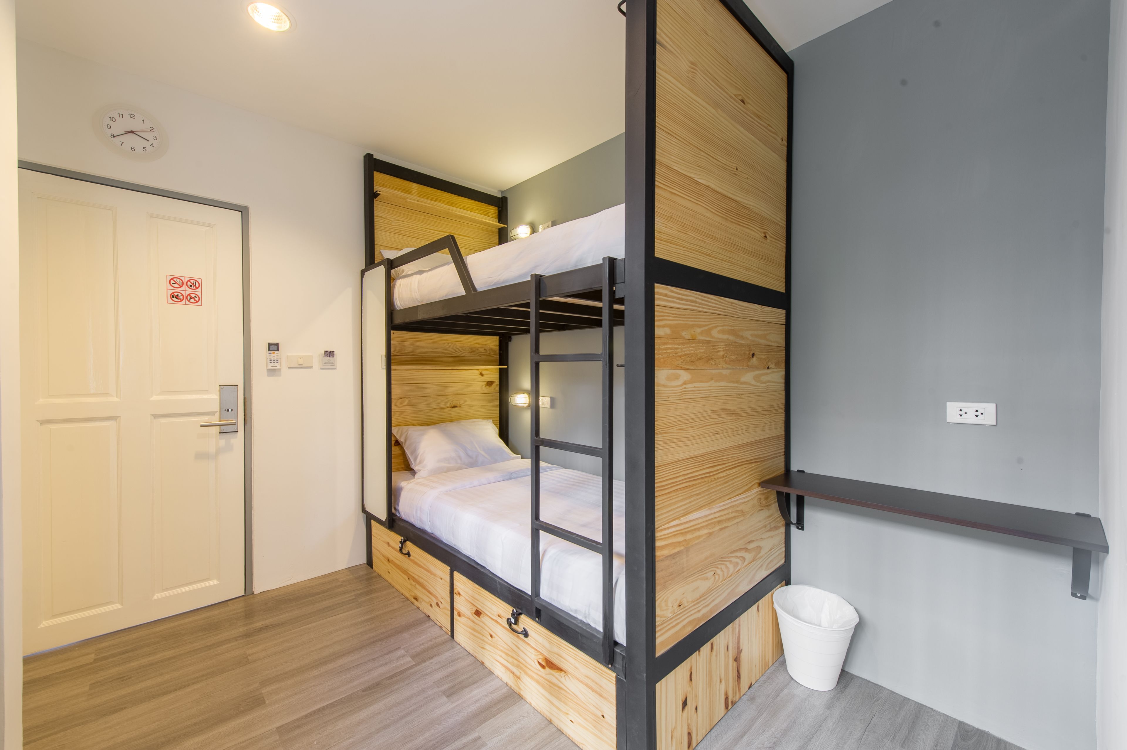 A bunk bed room with a wooden finish, a white door, a trash bin, and a wall-mounted shelf.