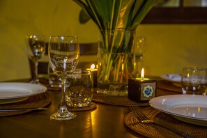 A dining table set with plates, glasses, and cutlery, accompanied by candles and a vase with green leaves. - Kurundu Villa (Habaraduwa)
