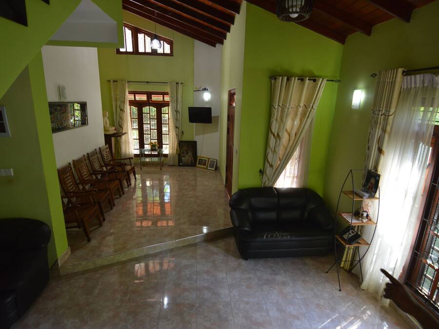 A spacious living area with a tiled floor, a black sofa, wooden chairs, and a bookshelf.