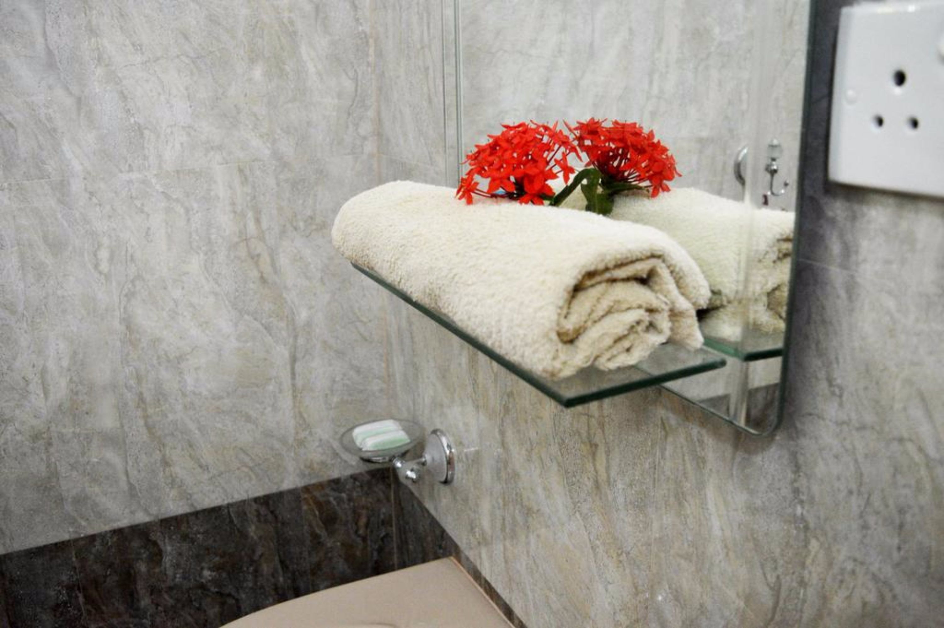 A bathroom with a glass towel rack holding folded towels and a vase with red flowers.