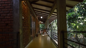 A covered corridor with brick walls, wooden flooring, and a railing overlooking a garden.