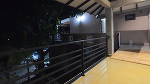 A covered outdoor area with a wooden floor, metal railing, and a view of a building with a light source.