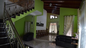 A spacious living area with a staircase, a black sofa, and a dining area with chairs.