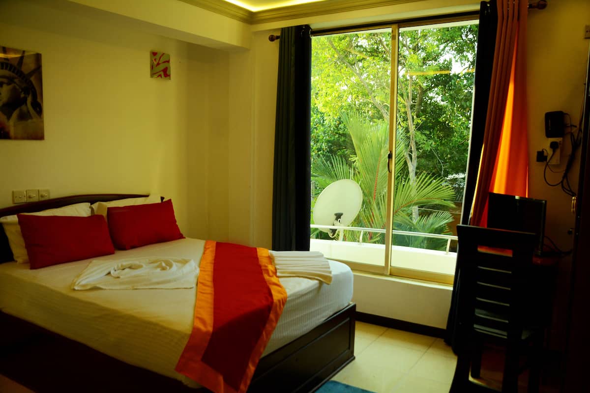 A hotel room with a bed, red pillows, a white towel, a window with curtains, and a chair.