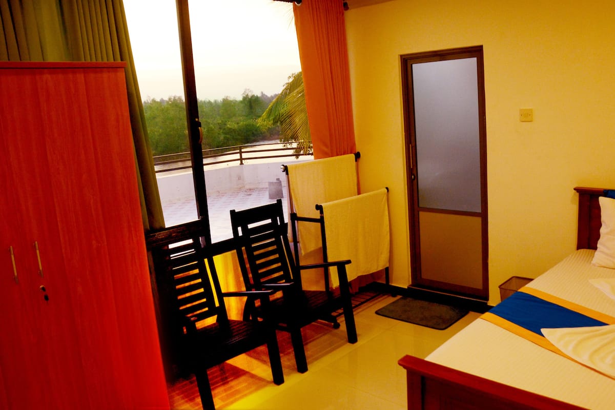 A hotel room with a bed, two chairs, a window with curtains, and a door.