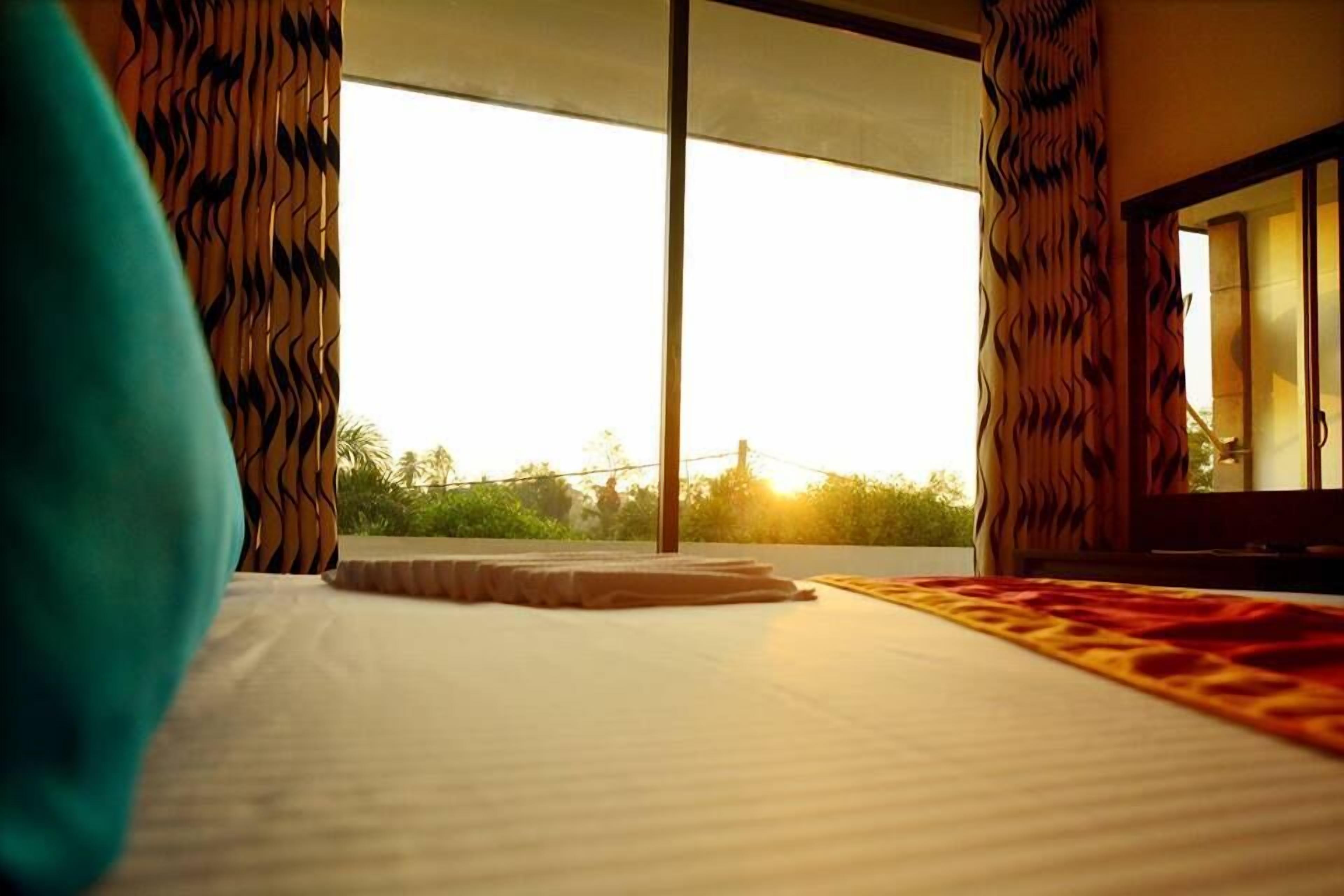 A hotel room with a large bed, a view of the outdoors, and curtains with a wavy pattern.