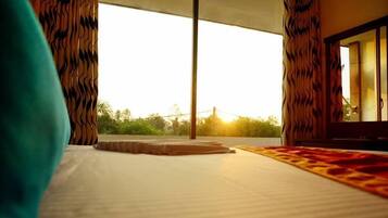 A hotel room with a large bed, a view of the outdoors, and curtains with a wavy pattern.