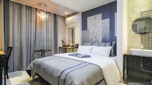 Une chambre d’hôtel comprenant un lit, un bureau, une chaise, une petite table ronde, un miroir et une salle de bain avec un lavabo et une douche.