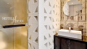 L’intérieur d’un hôtel au design moderne, comprenant un motif géométrique sur un mur, un miroir rond et un lavabo au style minimaliste.