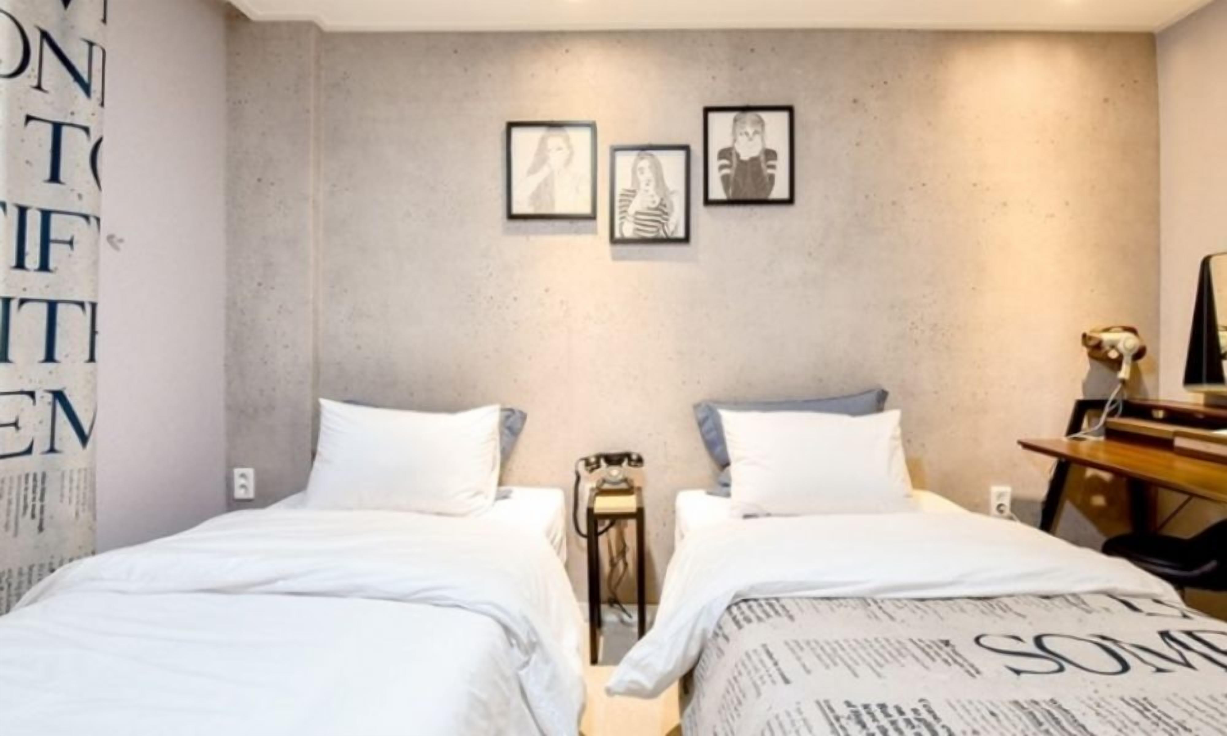 Habitación de hotel con dos camas, una mesita y un espejo. En la pared, hay cuadros enmarcados.