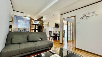 A modern living room with a grey sofa, a glass coffee table, and a dining area in the background.