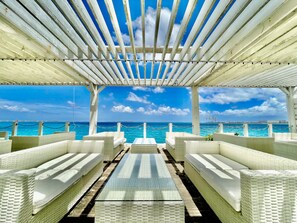 A covered outdoor seating area with white wicker furniture and a view of the ocean. - Hotel Umizola (Naha)